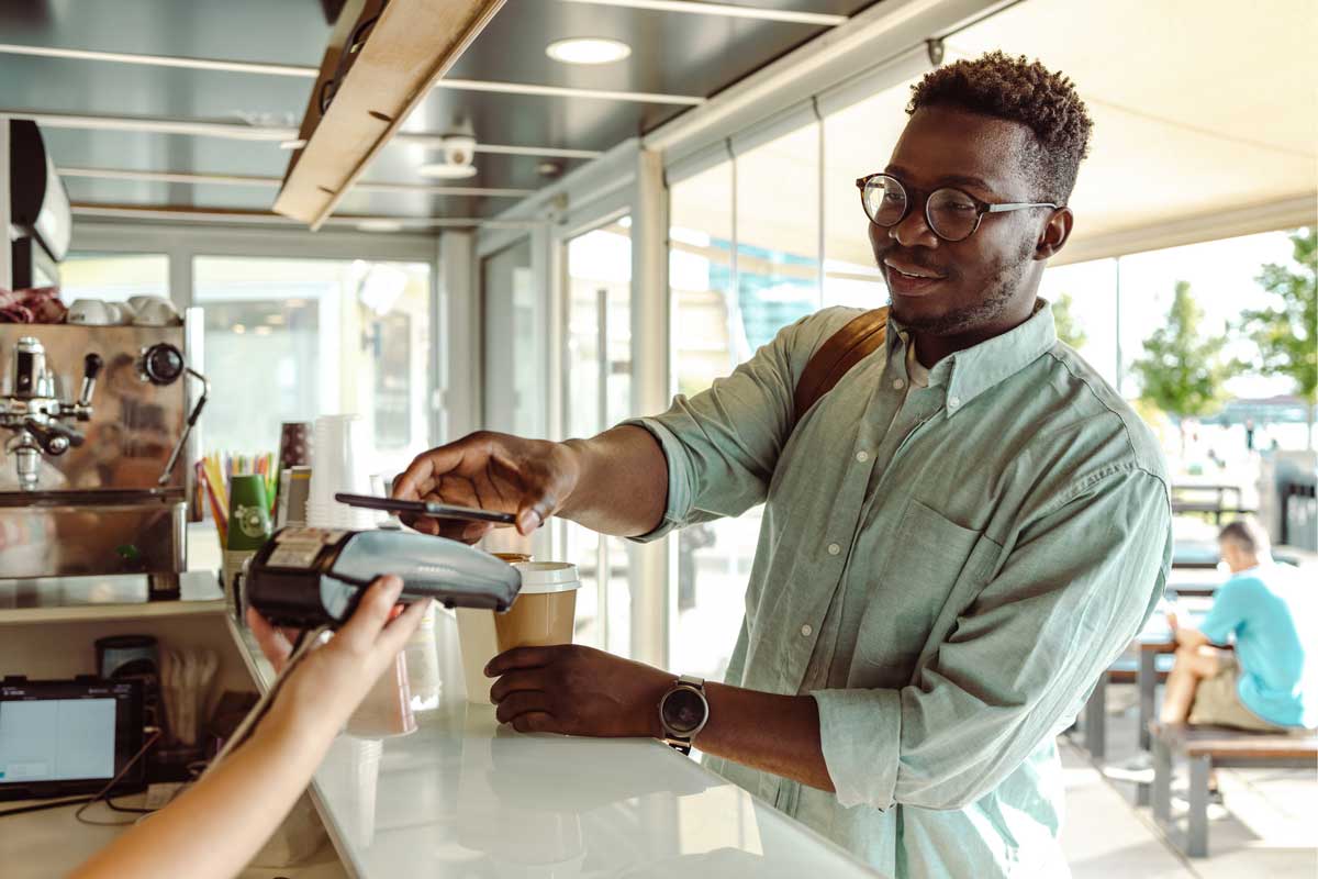 Junger afroamerikanischer Student zahlt einen Kaffee mit seinem Handy