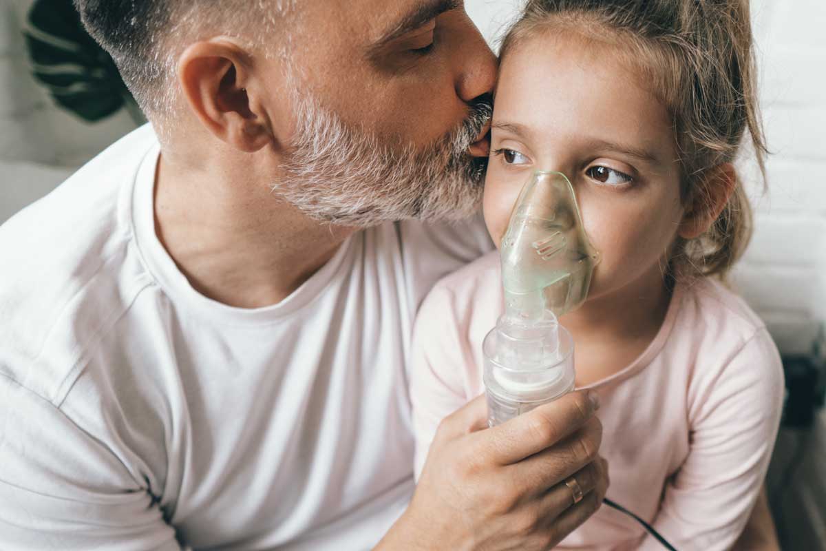 Vater hilft Tochter bei der Behandlung der Atemwege mit einem Inhalationsgerät.